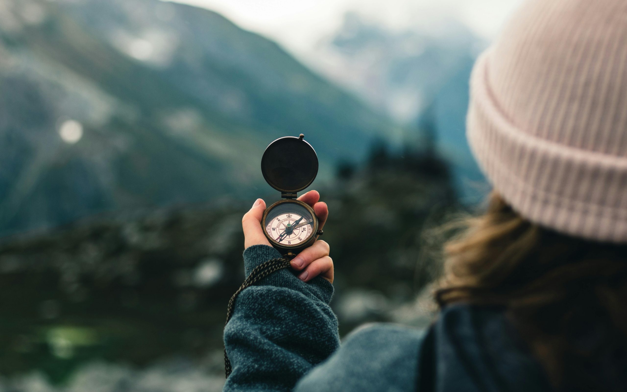 Colorful image of a hand holding a compass with mountains in the distance.