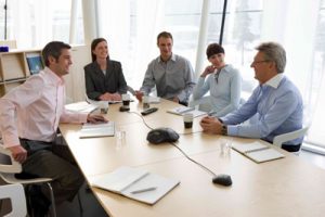 This image shows five adults sitting around a conference table. There are three adult men and two adult women.