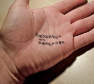 This is an image of a human palm lying face up on a desk. Written on the center of the palm in black ink is “Remember to remember