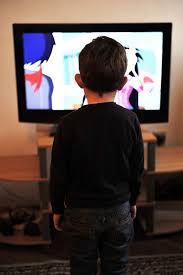 This image shows a little boy standing to watch television. He is facing away from the camera.