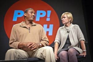 This image shows an adult Jennifer Thompson sitting next to Ronald Cotton. They are looking at each other while sitting on stage at Pop!Tech 2010 in Maine.