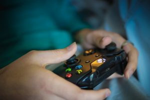 This image shows a close-up shot of a person playing a video game. The image shows two hands holding a black video game controller. The person has their right and left thumbs on two separate joy stick controllers.