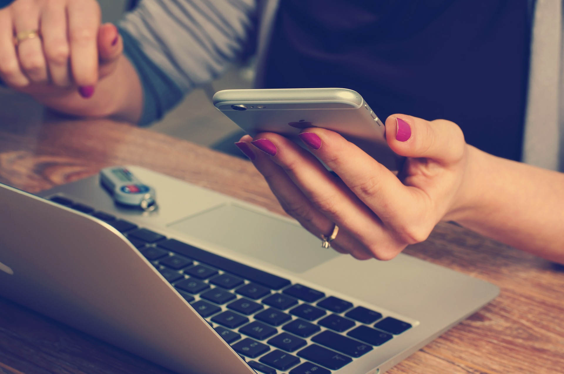 This is an image of a woman sitting at a table in front of a computer checking her cell phone