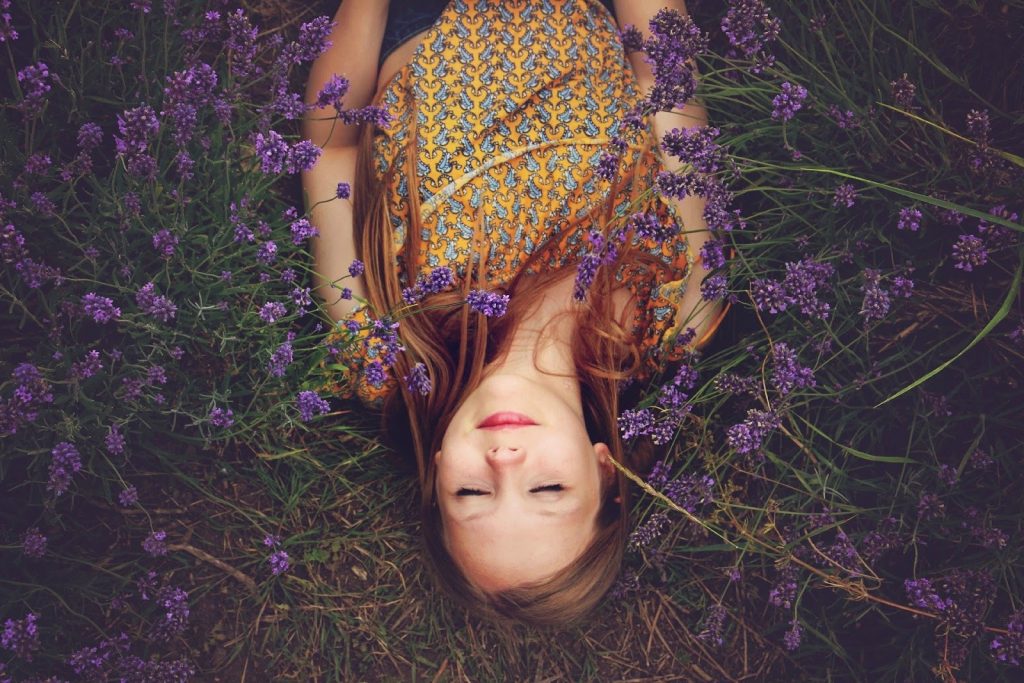 This is a color photograph of a woman lying in a field of lavender. The photo was taken from an aerial view.