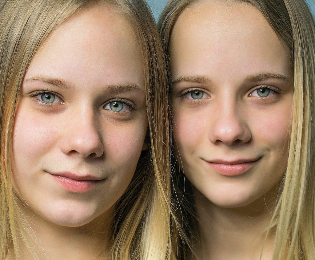 This image shows the faces of a set of adolescent, female, identical twins. They have long, blonde hair and blue eyes.