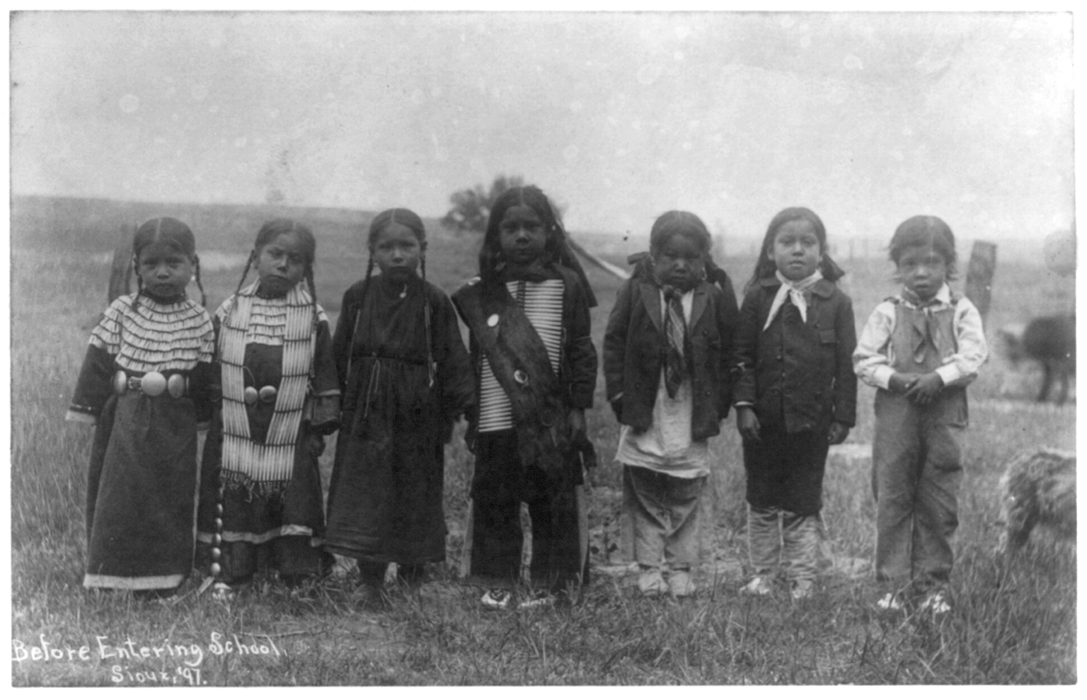 This is a black and white photograph of native children standing outside in a row.