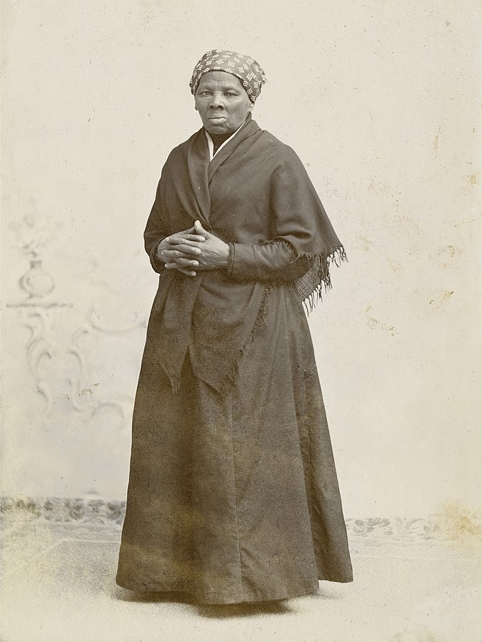 This is a black and white photograph taken of Harriet Tubman. She is standing in the photo with her hands intertwined against her sternum.