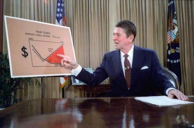 Ronald Reagan, seated in the Oval Office before a graph outlining income and taxation rates, gives a televised address explaining to the public his plan for reducing taxes.