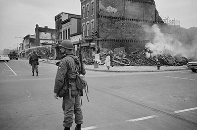 black and white image of smoking rubble and army man at the intersection of 7th and n streets in washington dc riots