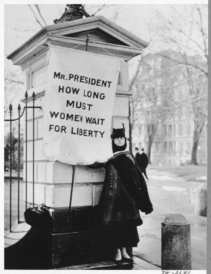 Flag Bearer For Women’s Rights Standing Near the White House, 1920. Flag reads, ‘Mr. President - How long must women wait for liberty?’