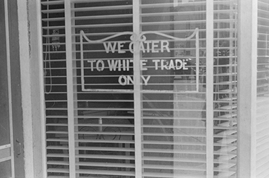 black and white image of storefront with words we cater to white trade only on the window